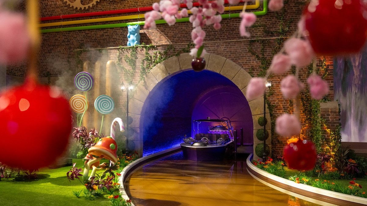 The chocolate river room on the set of Wonka's The Golden Ticket, with a candy-lined tunnel, giant cherries and lollipops.