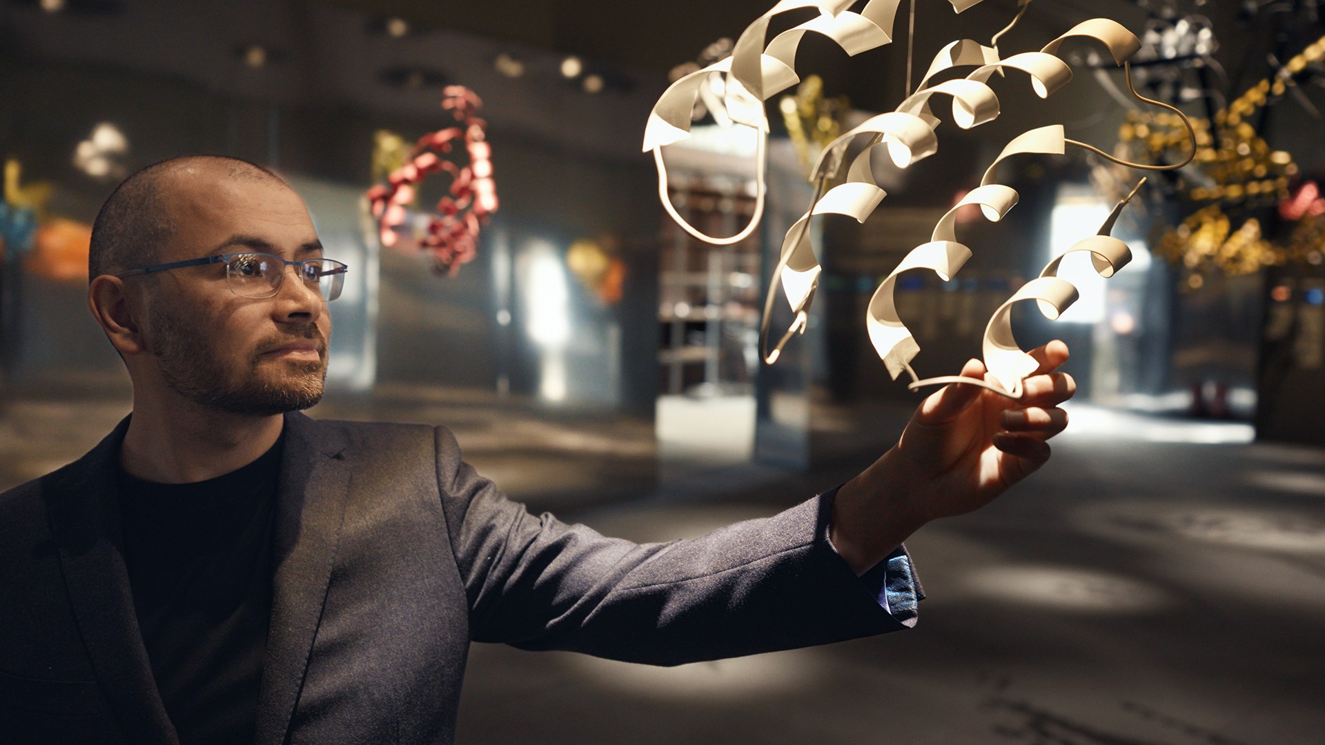 A man reaches toward suspended sculptures of protein structures in a still from the documentary The Thinking Game.