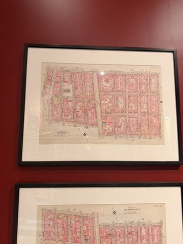 Two framed, hand-colored block maps of city lots in pink and yellow hanging on a dark red wall